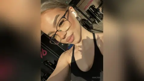 Smiling woman in black gym tank top taking a selfie in a bright fitness studio.