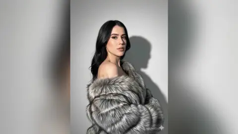 Elegant woman in a luxurious grey faux fur coat posing against a minimalist studio background.