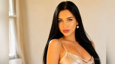 Beautiful woman with long dark hair wearing a champagne satin slip dress in a bright, minimalist room.