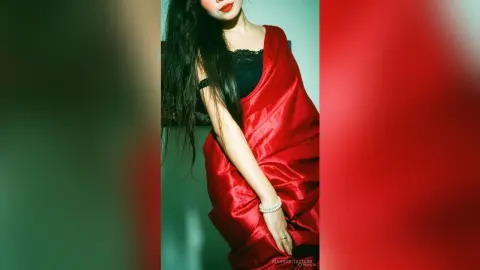 Elegant woman in a flowing red satin gown posing with a sophisticated mood in a studio setting.