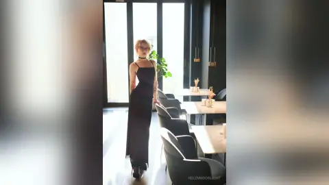 Elegant woman in a sleek black evening dress standing in a bright, modern minimalist dining room.