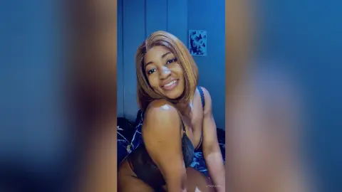 JoanJon smiles at the camera while wearing black lingerie in a blue room.