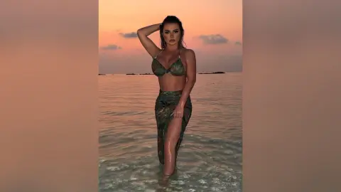 Woman in green patterned bikini and matching skirt standing in ocean water during a warm sunset.