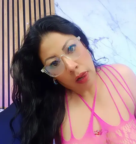 Woman with long dark hair and clear glasses wearing a pink strappy top in a bright modern room.