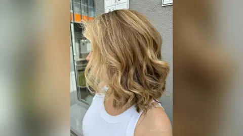 Side profile of a woman with wavy blonde hair wearing a white tank top in bright natural light.