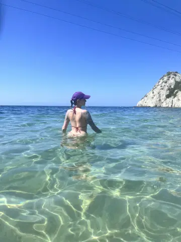 Young woman in a purple cap and bikini wading in clear turquoise ocean water on a sunny summer day.