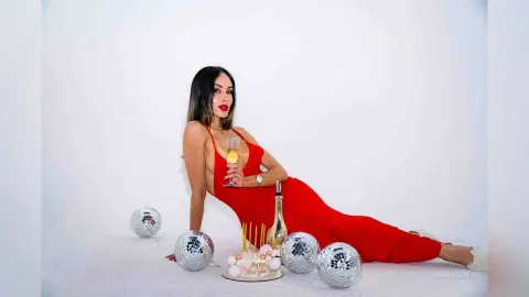 Elegant woman in a red evening gown holding champagne near disco balls for a festive New Year's Eve celebration.