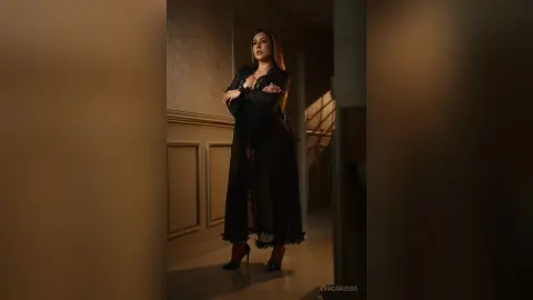 Elegant woman in a long black lace dress standing in a moody, dimly lit luxury hallway.