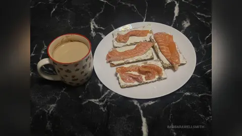 Smoked salmon cream cheese crackers on a white plate next to a cup of coffee on a black marble countertop.
