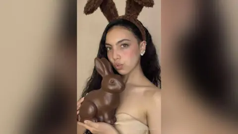 Young woman with bunny ears holding a large chocolate rabbit in a soft, festive Easter mood.