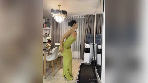 Elegant woman in a lime green strapless evening gown posing in a modern living room with a crystal chandelier.