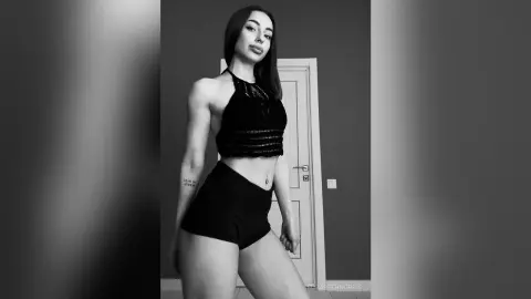 Athletic woman in black halter crop top and shorts posing in a modern minimalist room, black and white mood.
