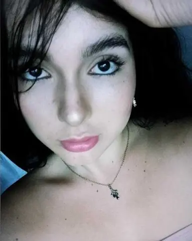 Close-up portrait of a young woman with dark hair and natural makeup wearing a delicate silver necklace.