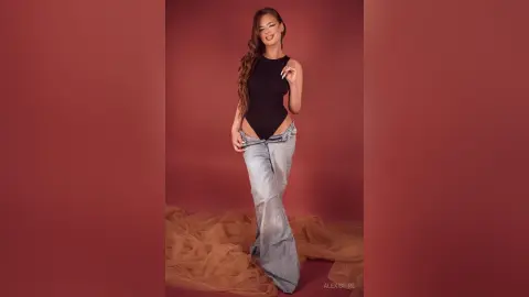 Fashionable woman in a black bodysuit and light wash denim jeans posing against a terracotta studio background.
