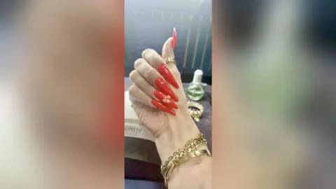 Close-up of long red stiletto nails with gold ring and jewelry in a luxury salon setting.