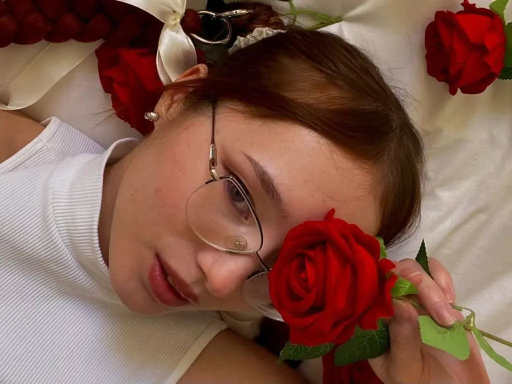 Young woman in a white turtleneck lying amidst red roses for a romantic and dreamy aesthetic portrait.