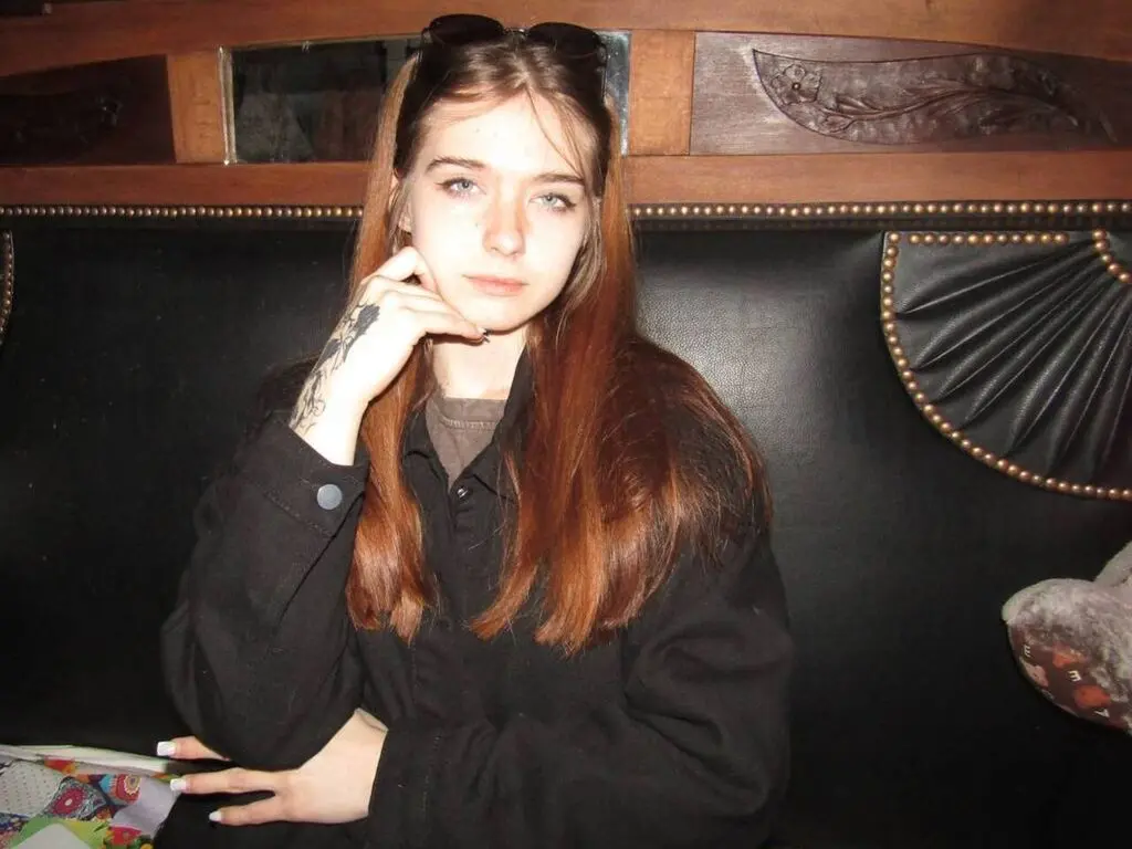 Young woman with long brown hair wearing a black jacket sitting in a dark vintage booth.