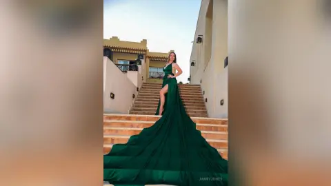 Elegant woman in a long emerald green gown posing on grand stone stairs of a luxury villa at sunset.