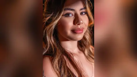 Smiling young woman with wavy brown hair in warm, golden sunlight for a glowing portrait.