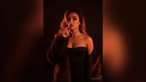 Glamorous woman in a black corset and fur coat posing in moody, warm studio lighting.