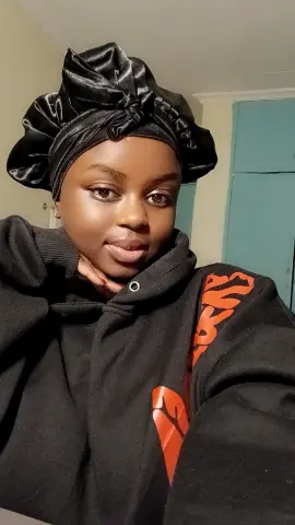 PrettyDoll22 wearing a black satin hair wrap and a black hoodie with red graphics, posing close-up in a room.