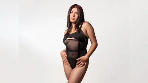 Young woman in a black sheer bodysuit posing against a white background for a minimalist fashion portrait.