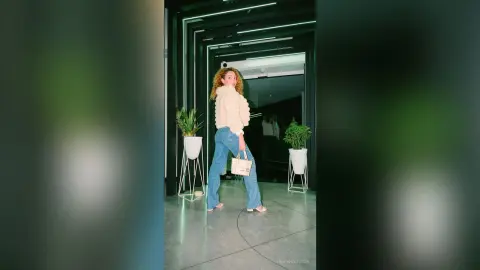 Stylish woman in a white fuzzy sweater and blue jeans standing in a modern minimalist interior with indoor plants.