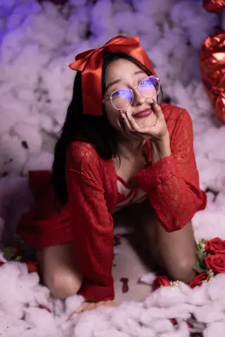 CloeLeee wears a red lace robe and a large red bow in her hair while kneeling among white fluffy clouds.