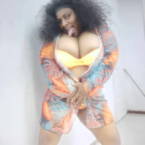 Curvy Black woman in a tropical floral robe and yellow bikini smiling playfully in a bright indoor setting.