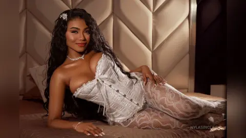 Beautiful woman in white lace lingerie relaxing on a bed in a luxurious, warm bedroom setting.