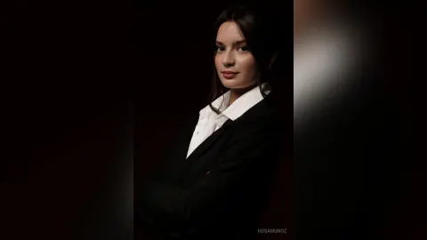 Elegant woman in a black blazer and white shirt posing with a sophisticated mood against a dark background.
