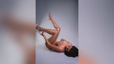 Fashionable woman in silver high heels posing gracefully on a grey studio background with a minimalist mood.