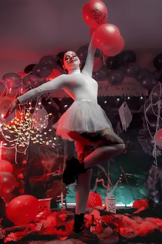 Woman in white outfit and tutu posing with red balloons in a spooky, moody Halloween setting.