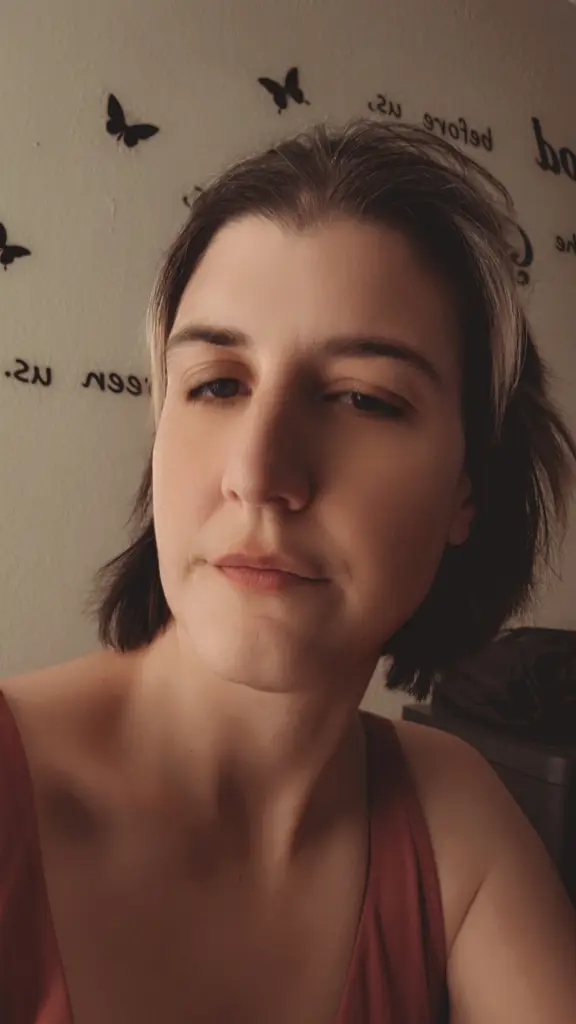 BellaWinters25 looks directly at the camera with a neutral expression, showing her face and dark hair against a plain white wall.