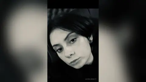Moody black and white portrait of a young woman with dark hair looking thoughtfully into the camera.