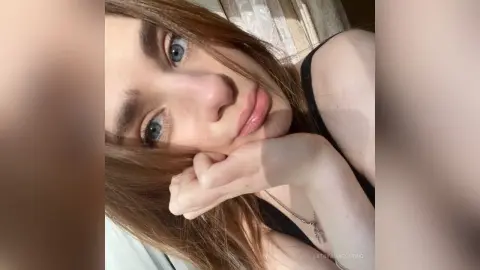 Close-up portrait of a young woman with long brown hair wearing a black tank top in soft natural sunlight.