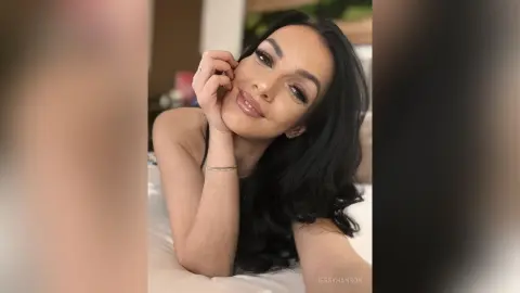 Smiling young woman with long dark hair relaxing in a bright bedroom setting.