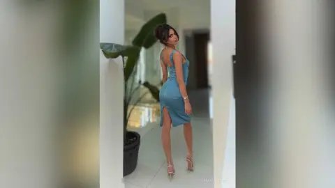 Elegant woman in a blue sleeveless midi dress posing in a bright modern room.