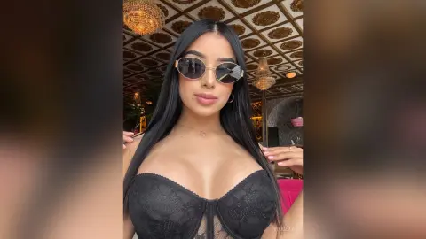 Young woman in black lace corset and sunglasses posing in a luxury hotel lobby with gold decor.