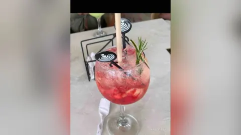 KattyLeya — KattyLeya presents a refreshing red fruit cocktail with ice and rosemary in a large glass on a marble table.