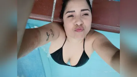 Smiling woman in a black bikini relaxing by a blue swimming pool on a sunny summer day.