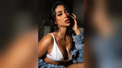 Glamorous woman in a white bikini top and denim jacket posing with a moody, sun-kissed glow.