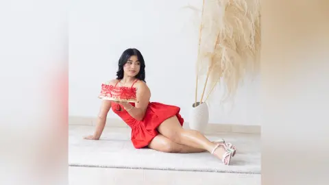 Smiling woman in a red summer dress sitting on a white rug in a bright, minimalist room.