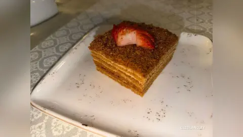 A slice of layered honey cake topped with a fresh strawberry slice on a white ceramic plate.
