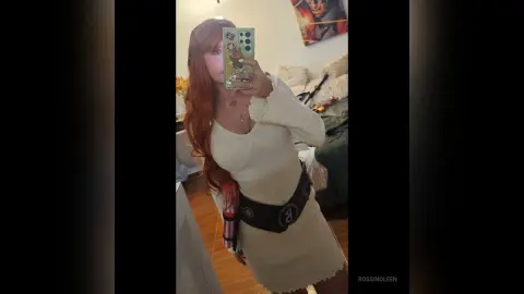 RossiNoleen poses in a white long-sleeved knit dress while holding a red vibrator against her stomach.
