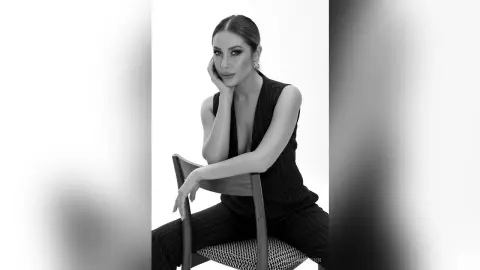 Elegant woman in a black sleeveless jumpsuit posing thoughtfully in a minimalist studio setting.