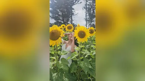Smiling woman in a white dress enjoying a sunny day in a vibrant sunflower field.