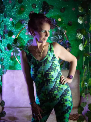 Woman in a green patterned jumpsuit sitting against a lush tropical leaf backdrop with dreamy lighting.