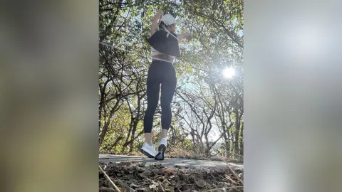 Athletic woman in black leggings and white sneakers posing in a sunny forest setting.