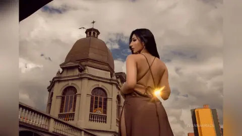 Elegant woman in a backless brown dress posing against a classical dome building under a cloudy sky.